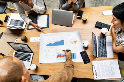 7 Overhead view of a team meeting around a table filled with laptops, coffee, and a large business chart.